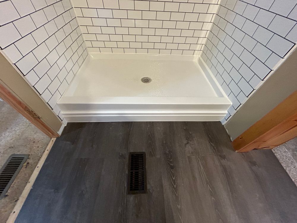 Shower stall with white subway tile, white shower pan, and gray flooring.