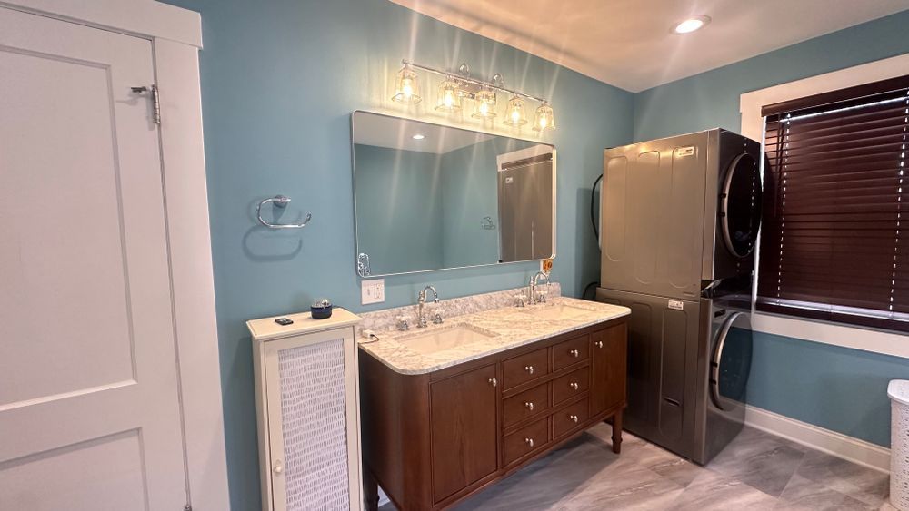 Bathroom with blue walls, vanity, stacked washer/dryer, and small window with blinds.