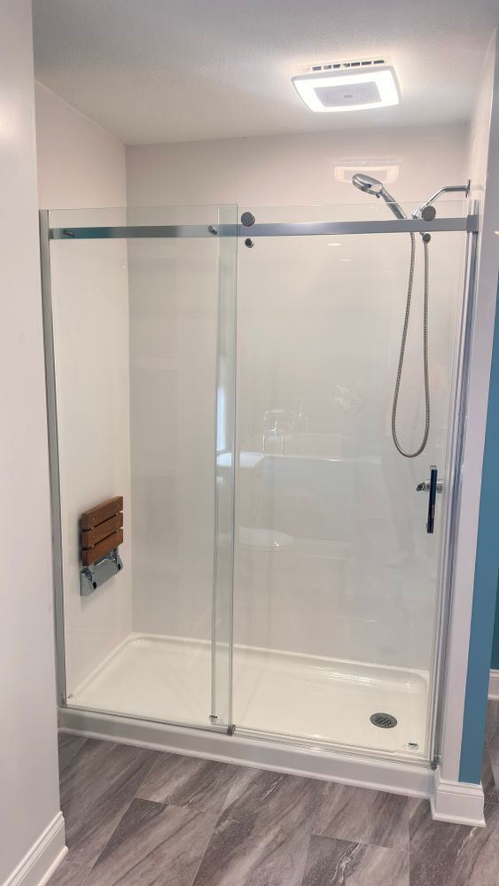Modern shower with sliding glass doors and a built-in bench. White walls and floor, chrome fixtures.