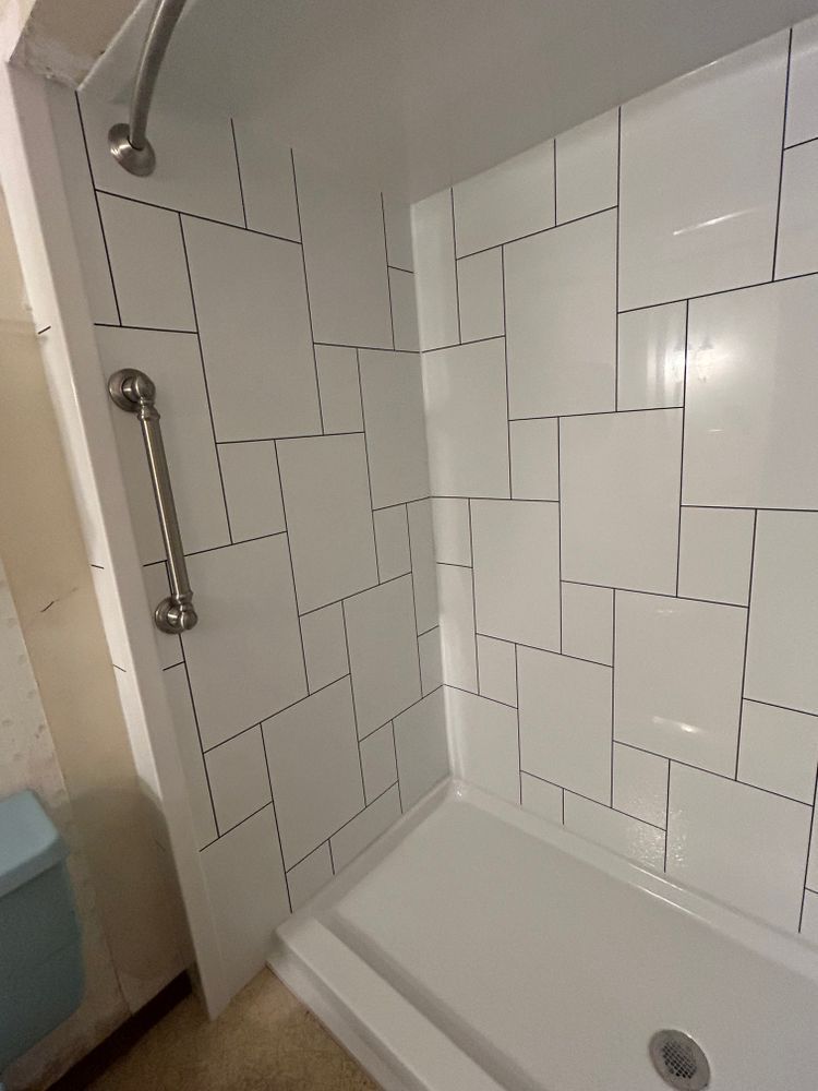 White tiled shower with a grab bar, in a bathroom.