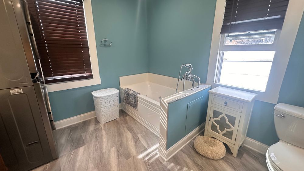Bathroom with blue walls, white tub, wood blinds, and gray flooring.