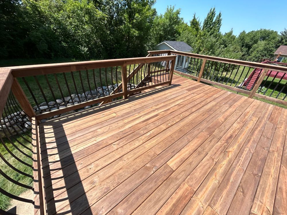 Wooden deck with black railings, overlooking a green yard on a sunny day.