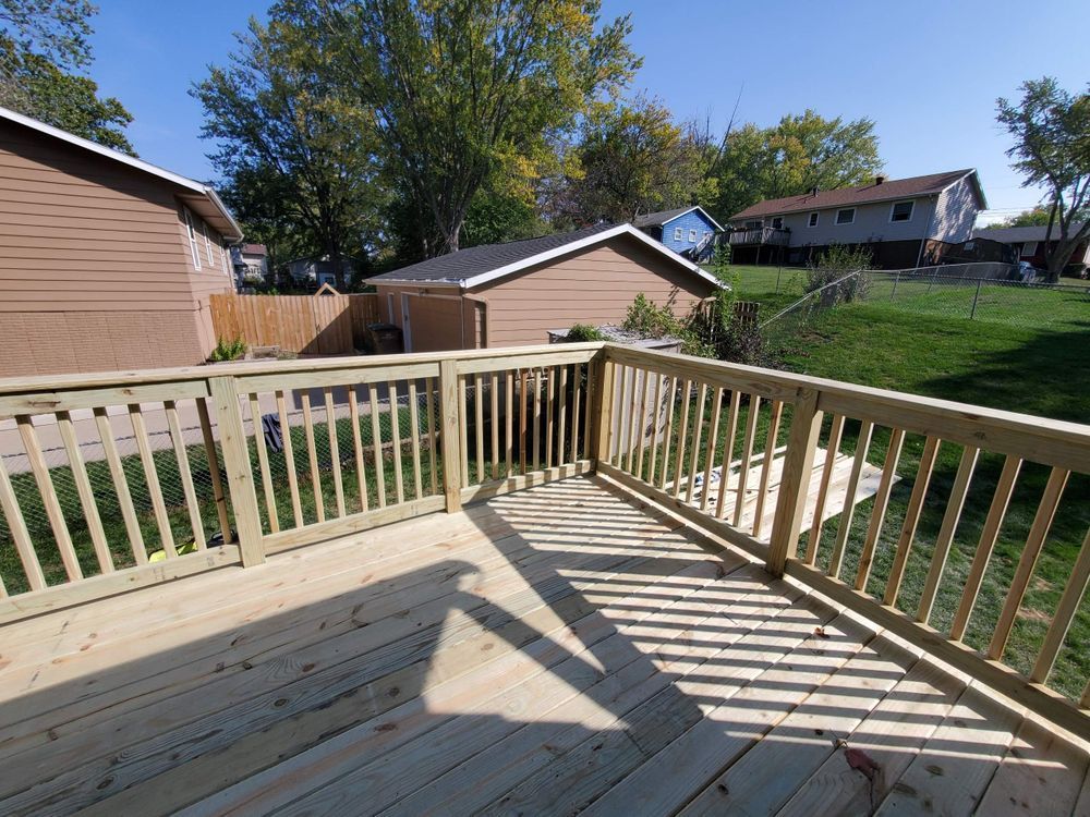 Wooden deck with railings in a backyard. Houses and green grass in the background on a sunny day.