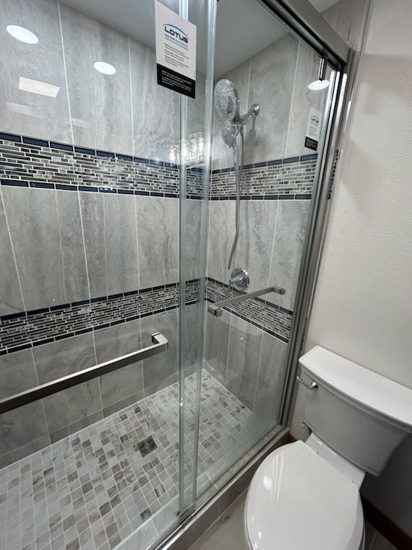 Shower with gray and blue tile, glass door, and a toilet.