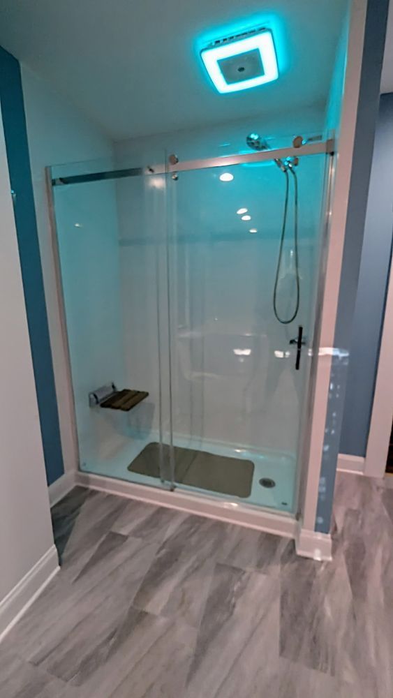 Modern shower with glass doors, a built-in bench, and a rainfall showerhead. Blue walls and gray flooring.