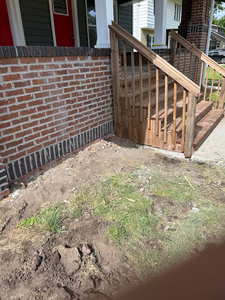 Brick exterior of a house with wooden stairs and a small patch of dirt and grass.