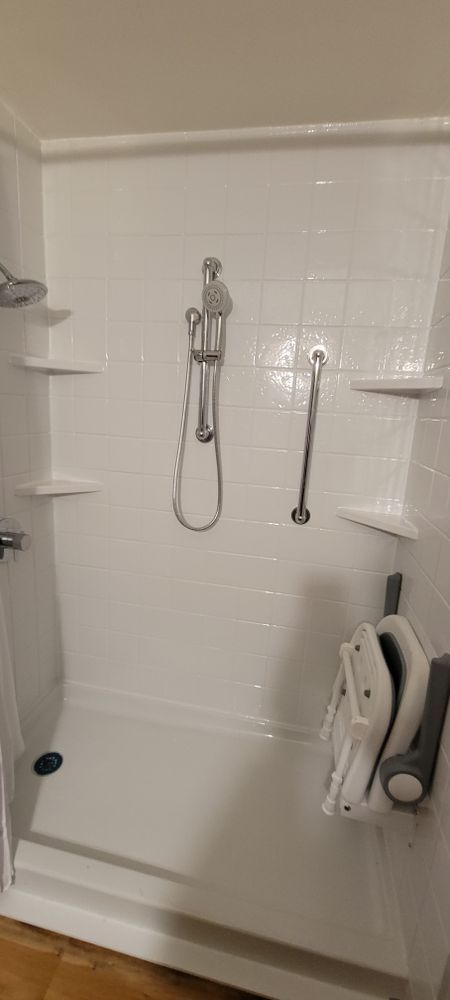 White accessible shower with a foldable seat and grab bar.