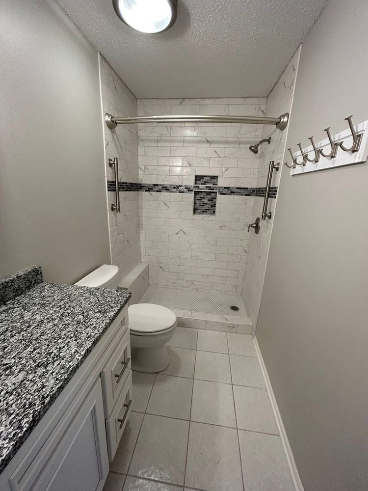 Small bathroom with white tile shower, toilet, vanity with granite countertop.