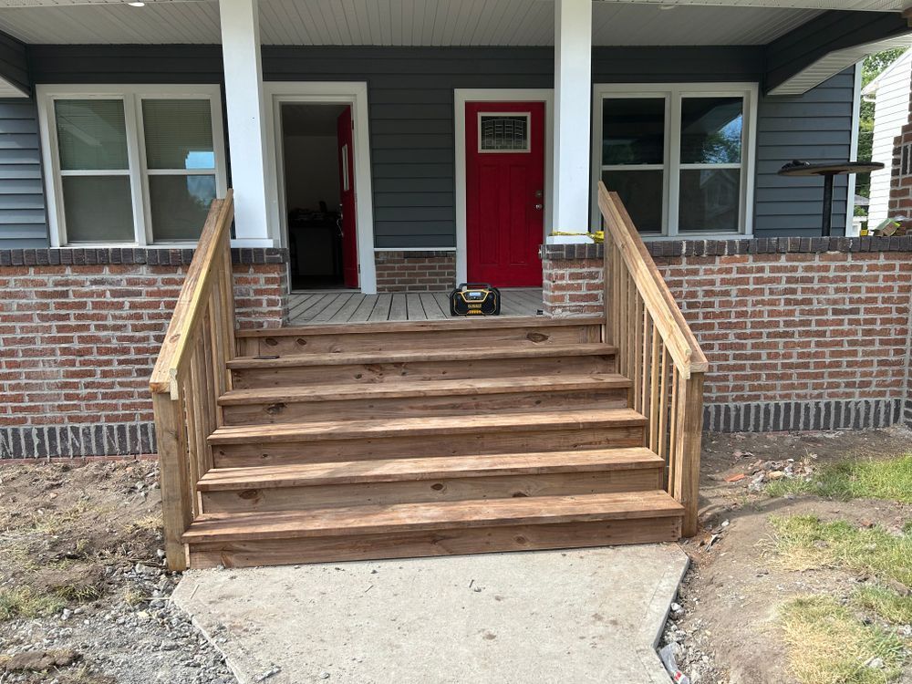 Wooden stairs leading to a porch with red doors and brick and gray siding.