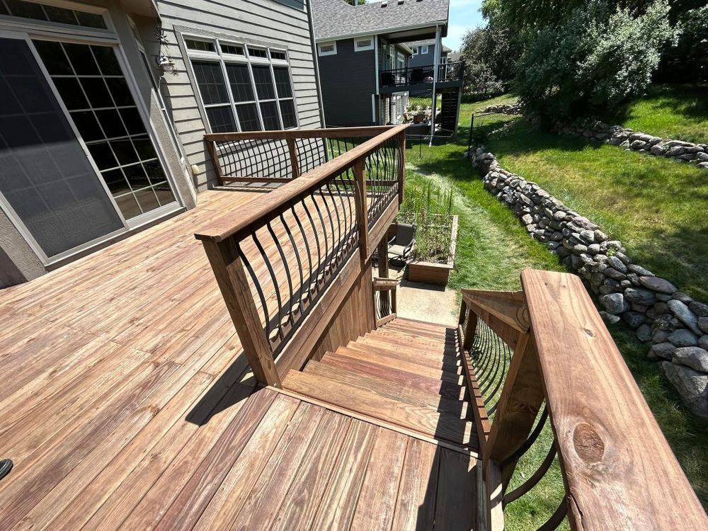 Wooden deck with stairs leading down to a lower level; railing, grass, and a retaining wall are visible.