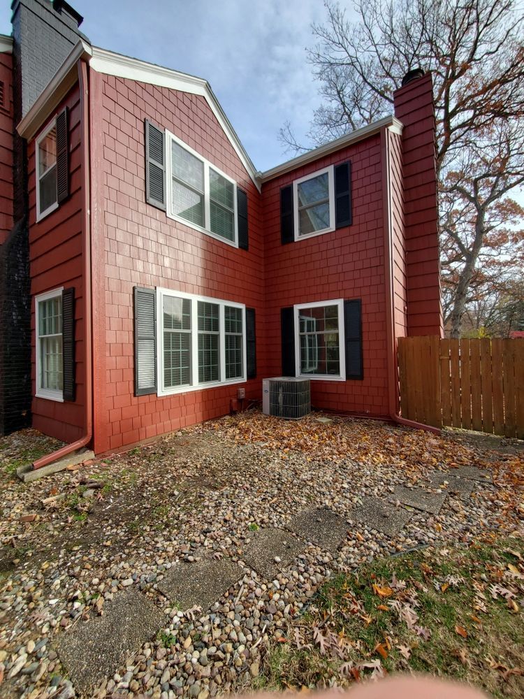 Red-sided townhouse with black shutters, windows, and chimney on a fall day, surrounded by fallen leaves.