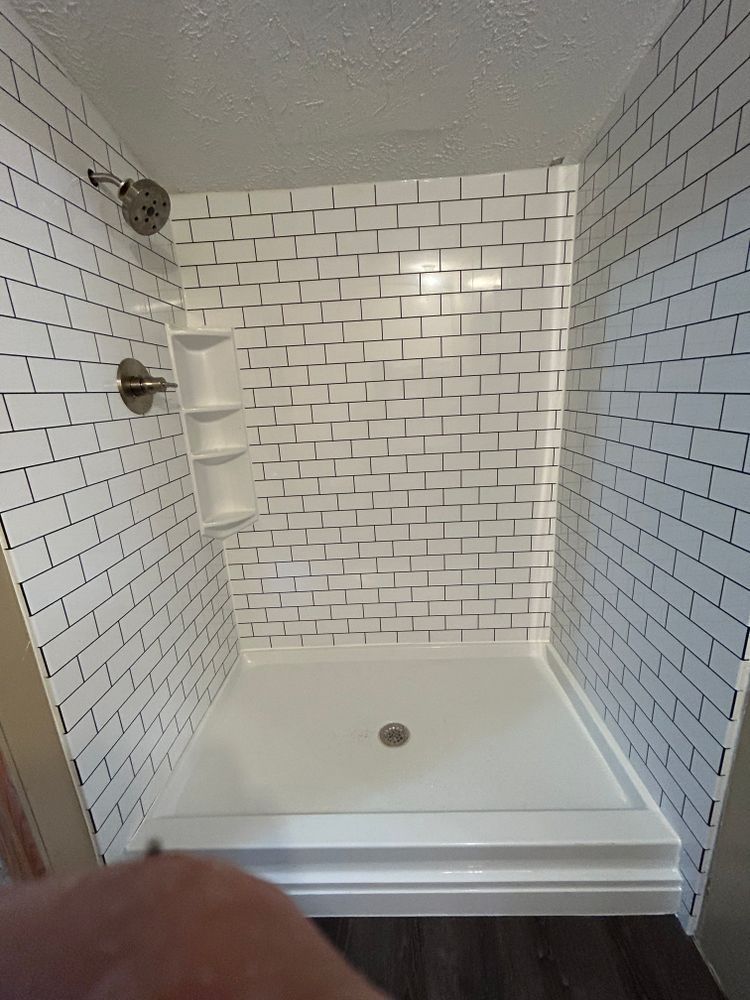 White-tiled shower stall with a built-in soap/shampoo caddy and a silver showerhead.