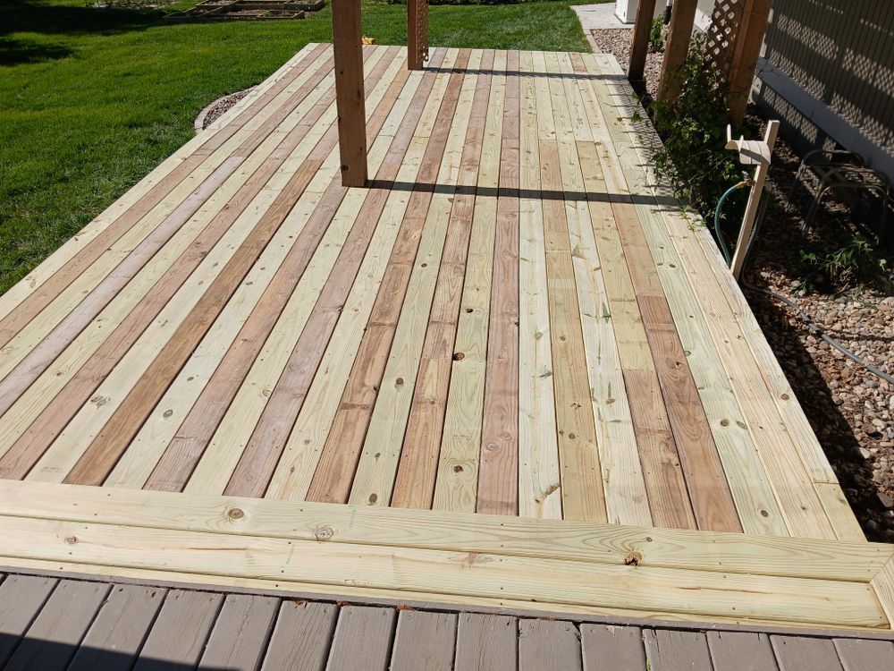 Wooden deck with vertical planks, posts, and a border, in a yard setting.