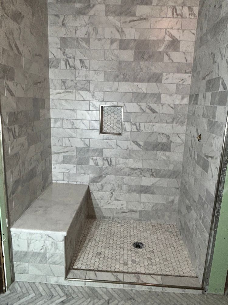 Tiled shower with built-in bench and niche. Grey marble-like tiles and a mosaic tile floor.