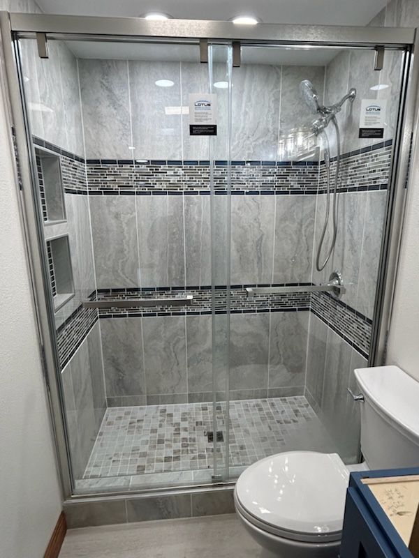 Shower stall with gray and mosaic tiles, glass door, and a toilet.