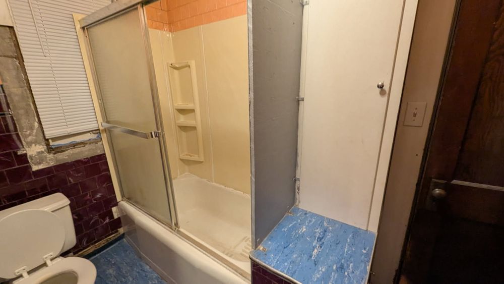 Bathroom with a toilet, shower, and cabinet. Blue floor, pink and orange walls.