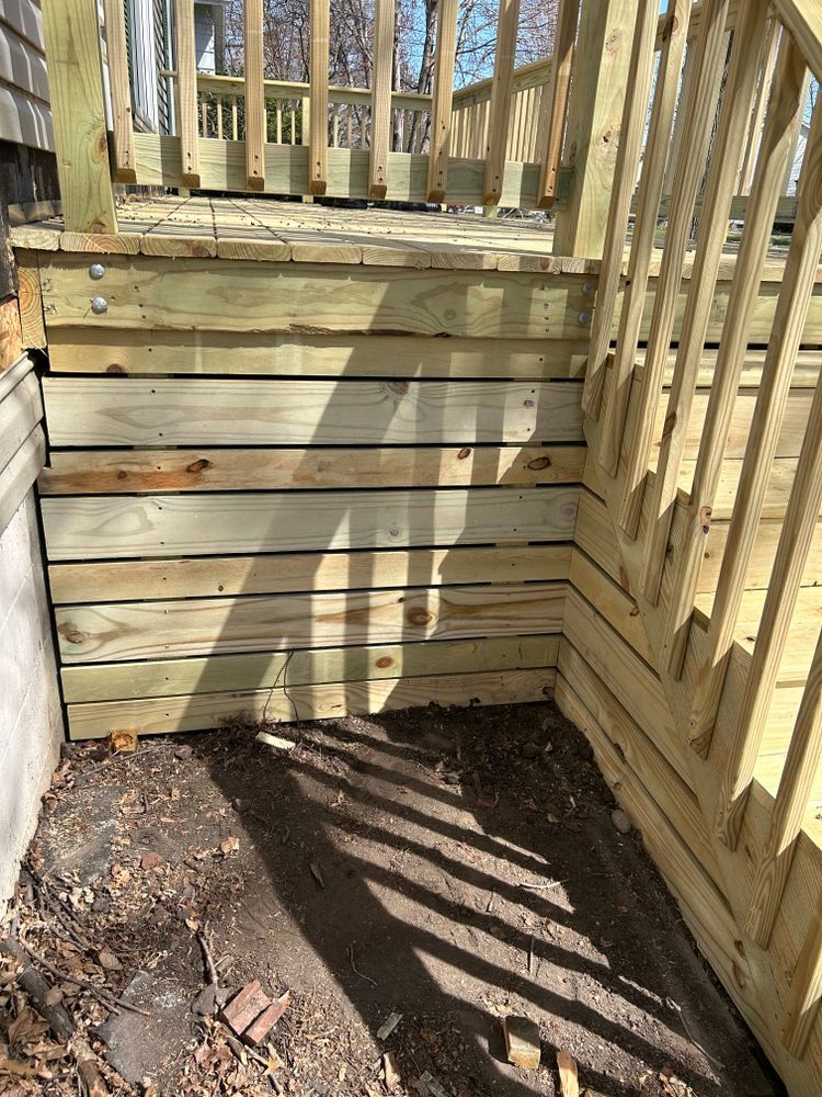 Wooden deck with stacked wood siding. Brown dirt and shadows below.