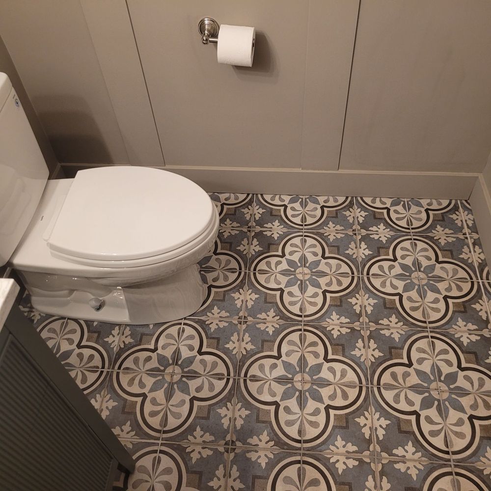 Toilet in a bathroom with gray patterned floor tiles and gray walls.