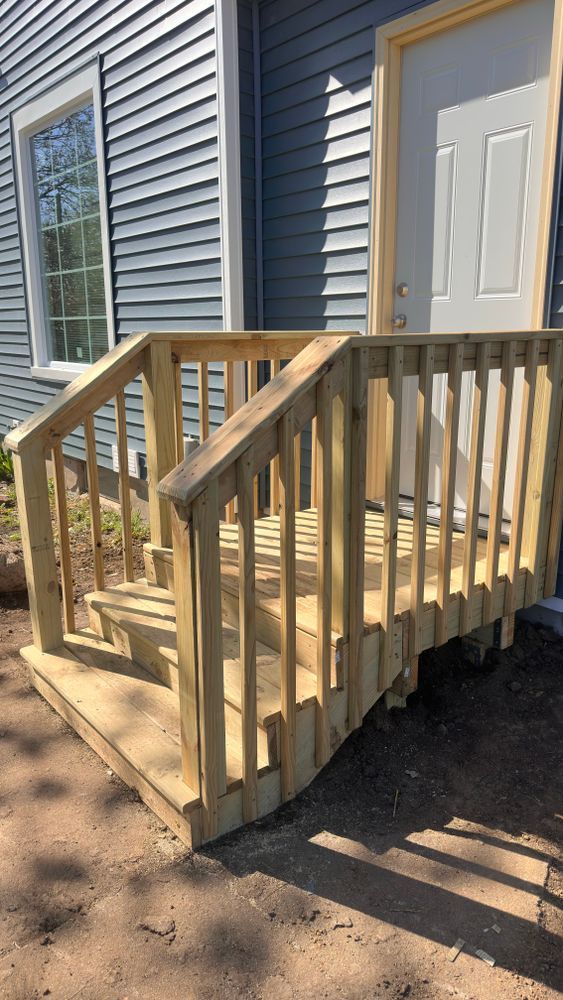 Wooden steps leading to a blue house with a white door. Natural wood railings and stairs.