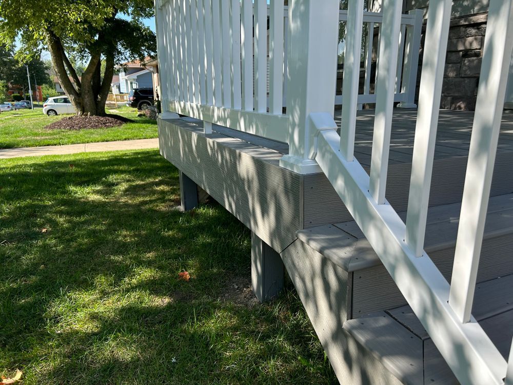 White railing on a gray composite deck with concrete base in front yard on a sunny day.