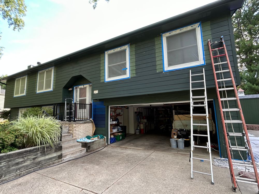 Green house exterior being painted; ladders, garage, and front steps are visible.