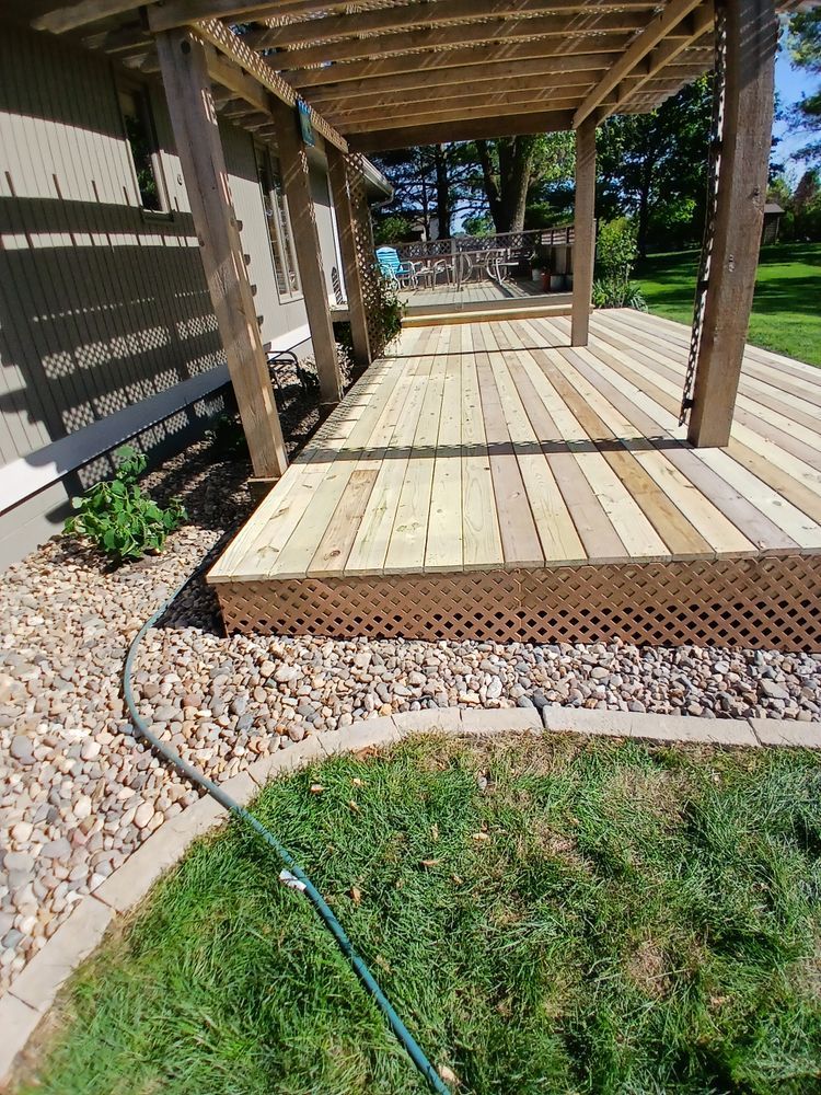 Wooden deck with pergola, lattice skirt, bordering a grassy yard and rock bed.