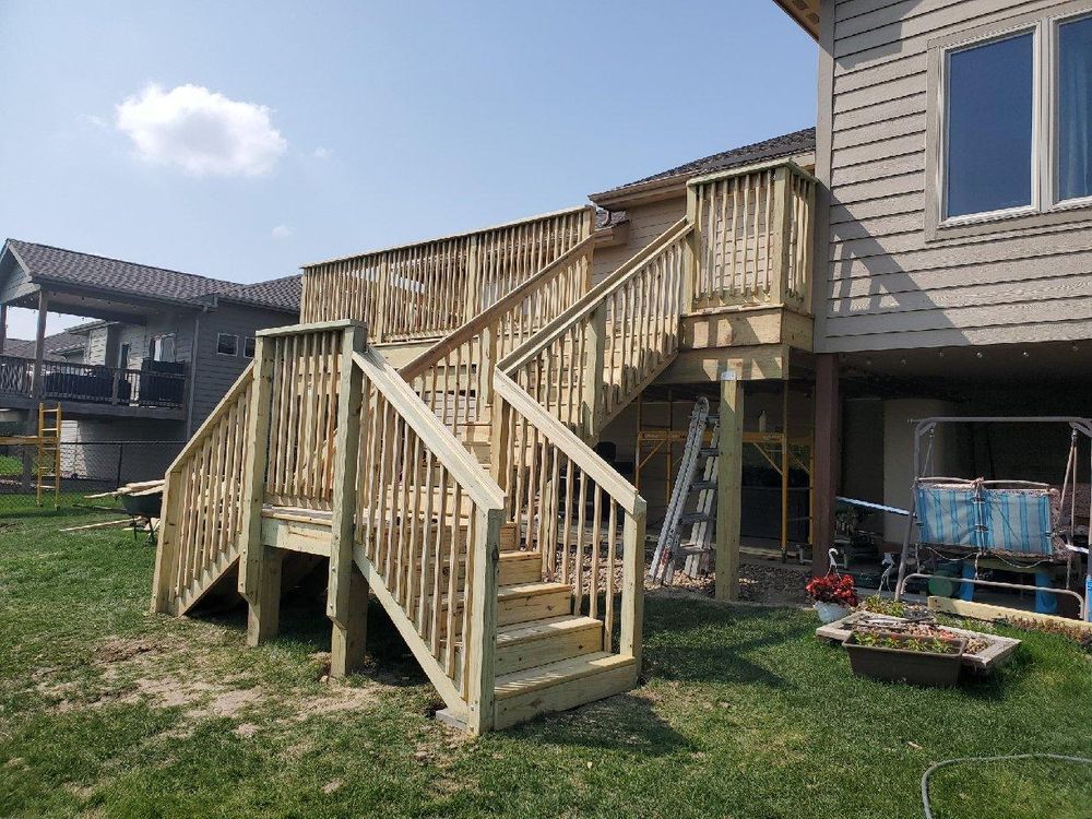 Wooden deck with stairs, attached to a house with tan siding, built on a grassy lawn.
