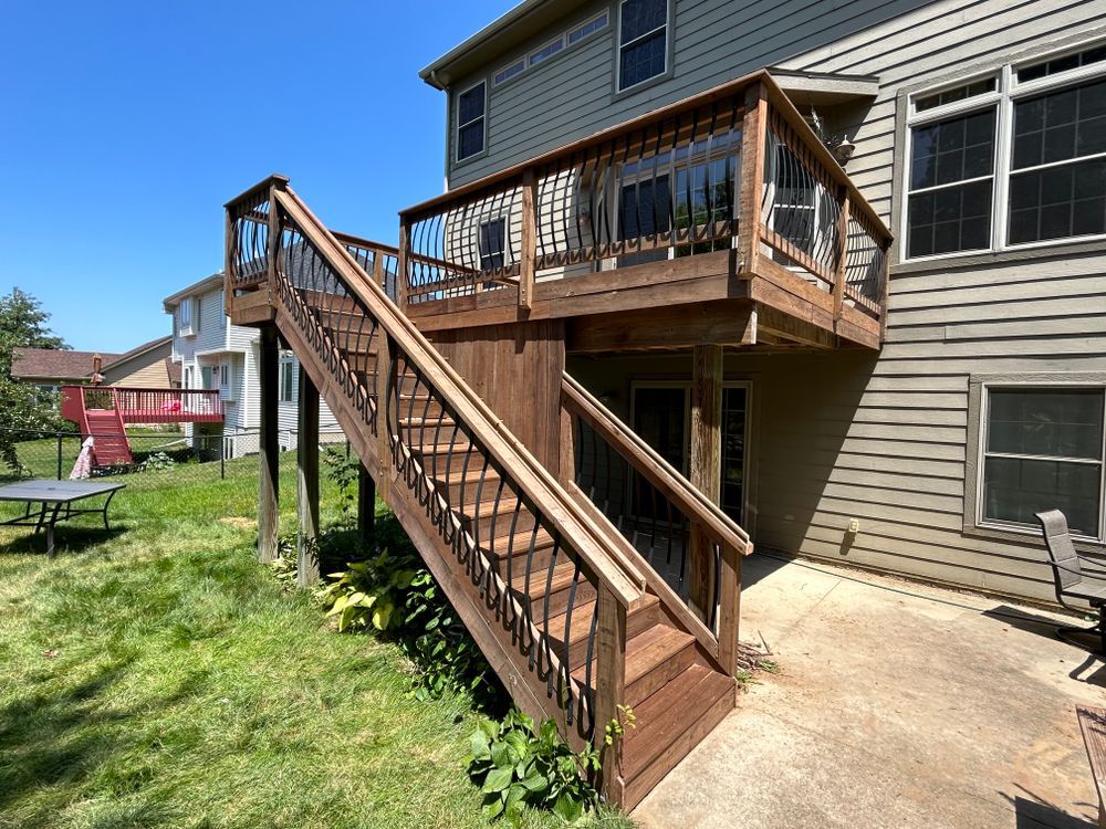 Wooden deck with stairs attached to a two-story house, sunny day.