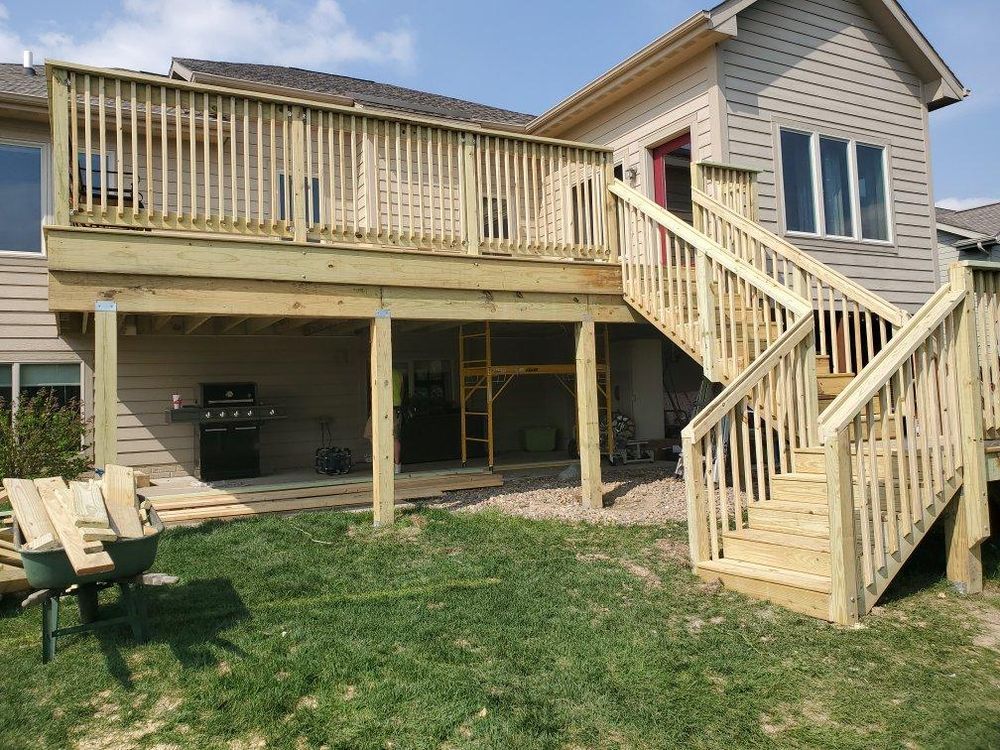 A two-level wooden deck under construction next to a house with grass in the foreground.