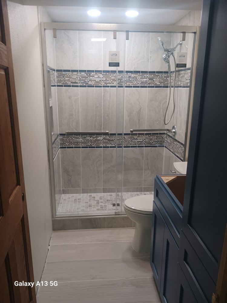 Bathroom with glass shower, blue vanity, and gray tiled walls and floor.