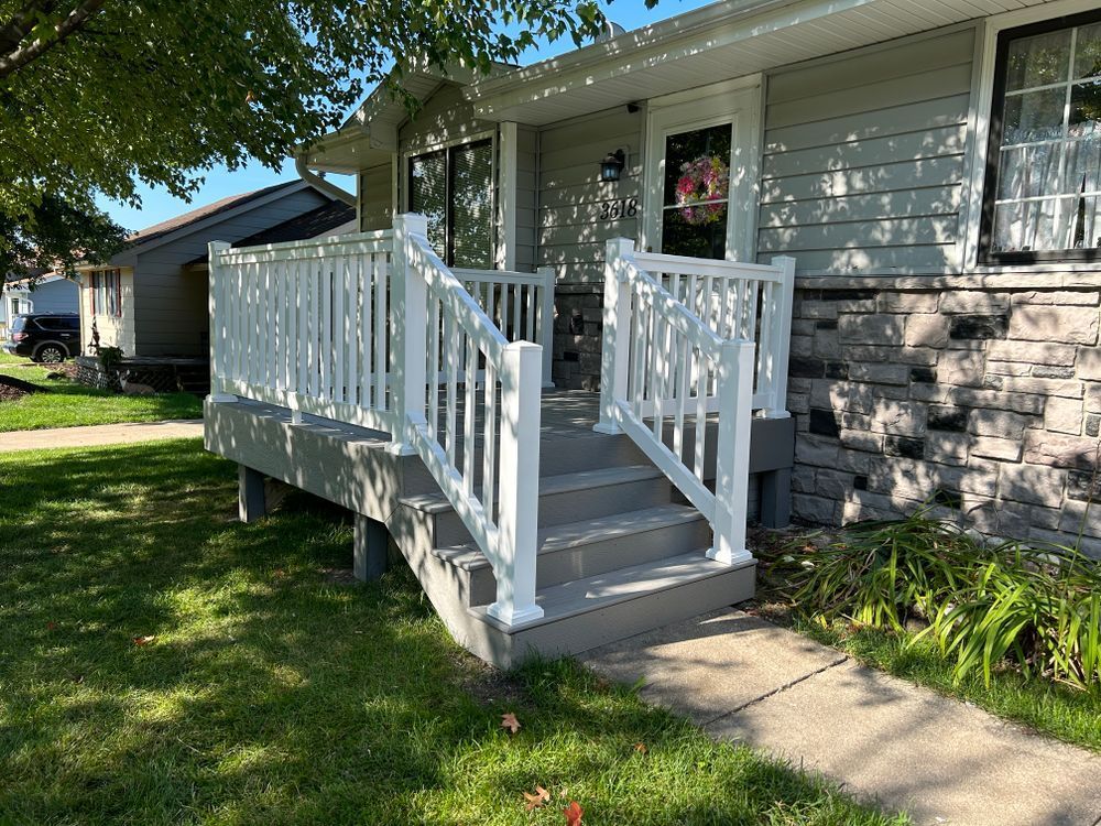 White-railed porch with steps leading to a house with gray siding and stone accents. Green grass and path in foreground.