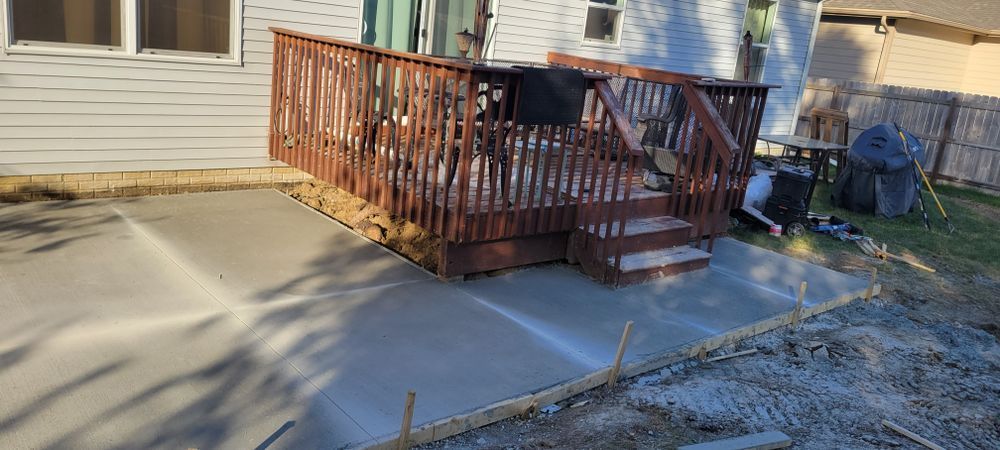 A newly poured concrete patio next to a wooden deck, next to a house.