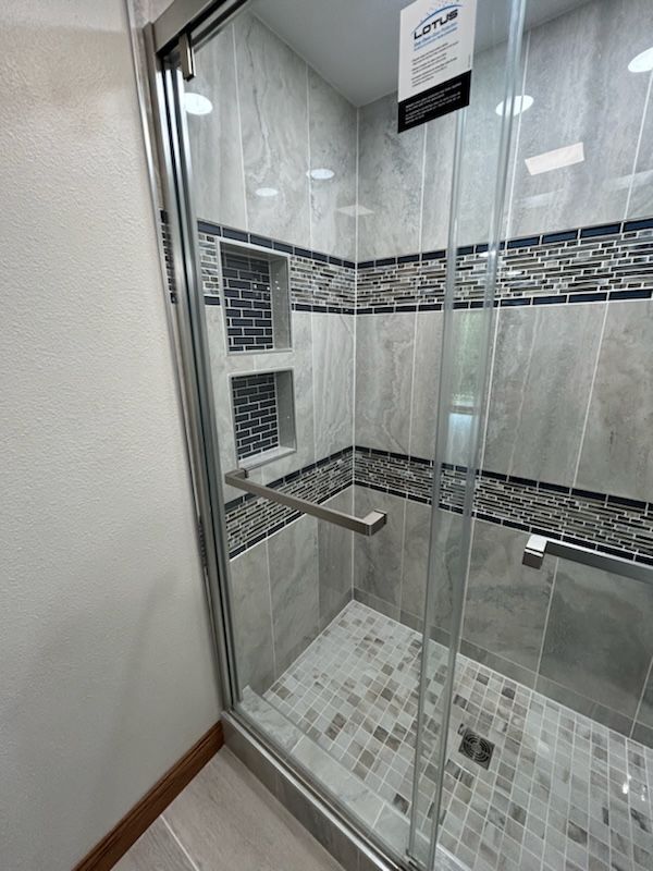 Modern shower with glass door, grey tile walls, mosaic accent, and two built-in niches.