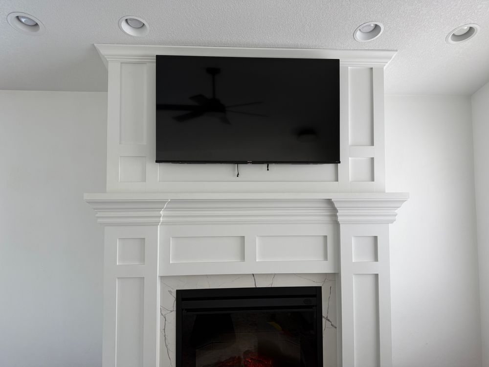 White fireplace with a mounted TV above, set against a white wall; the TV is turned on.