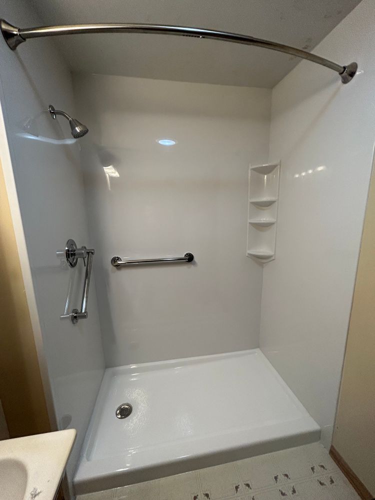 White, accessible shower with a curved shower rod, grab bar, and built-in shelves.