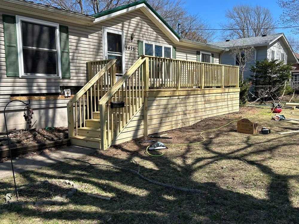 Wooden deck with steps and railing leading to the front door of a beige house with green shutters.
