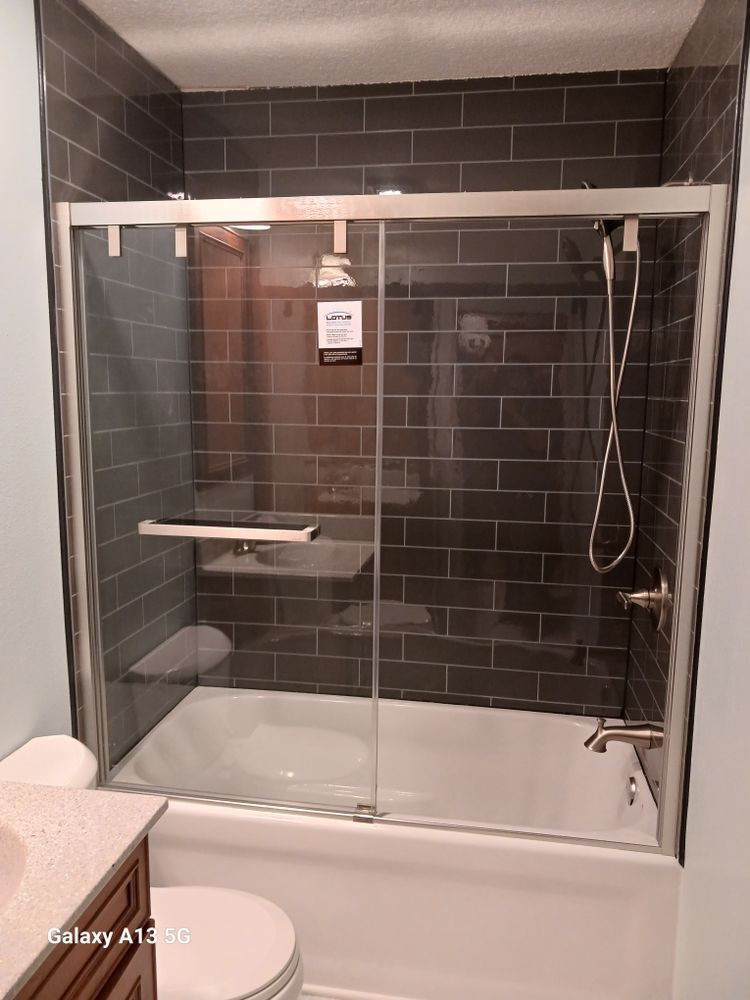 A bathroom with a white tub, glass shower doors, dark gray tile, and brushed nickel fixtures.