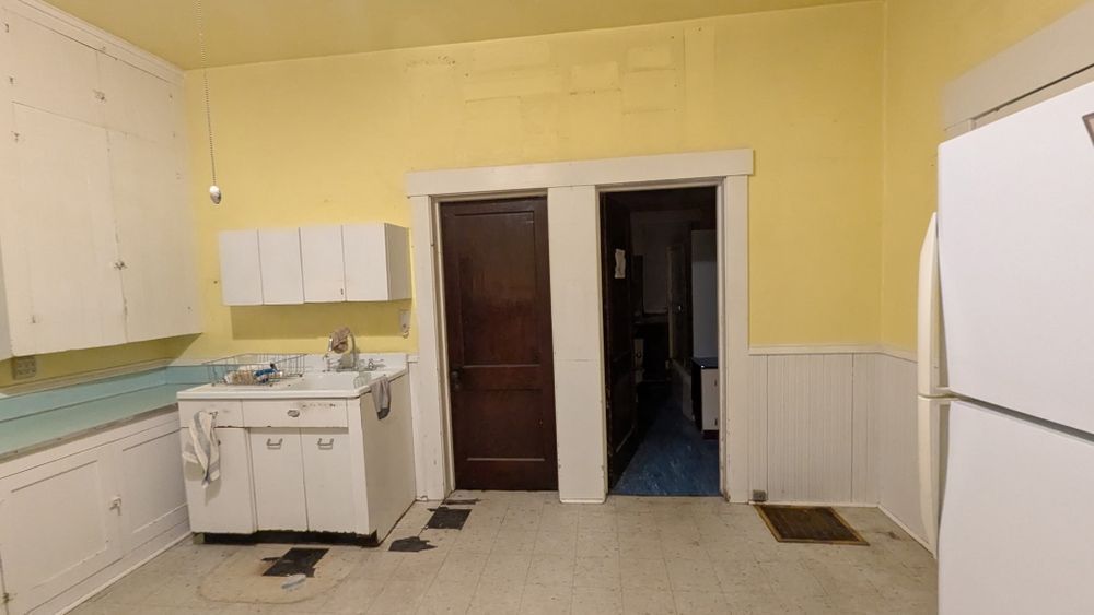 A kitchen with yellow walls, white cabinets, and a dark wooden door leading to another room.