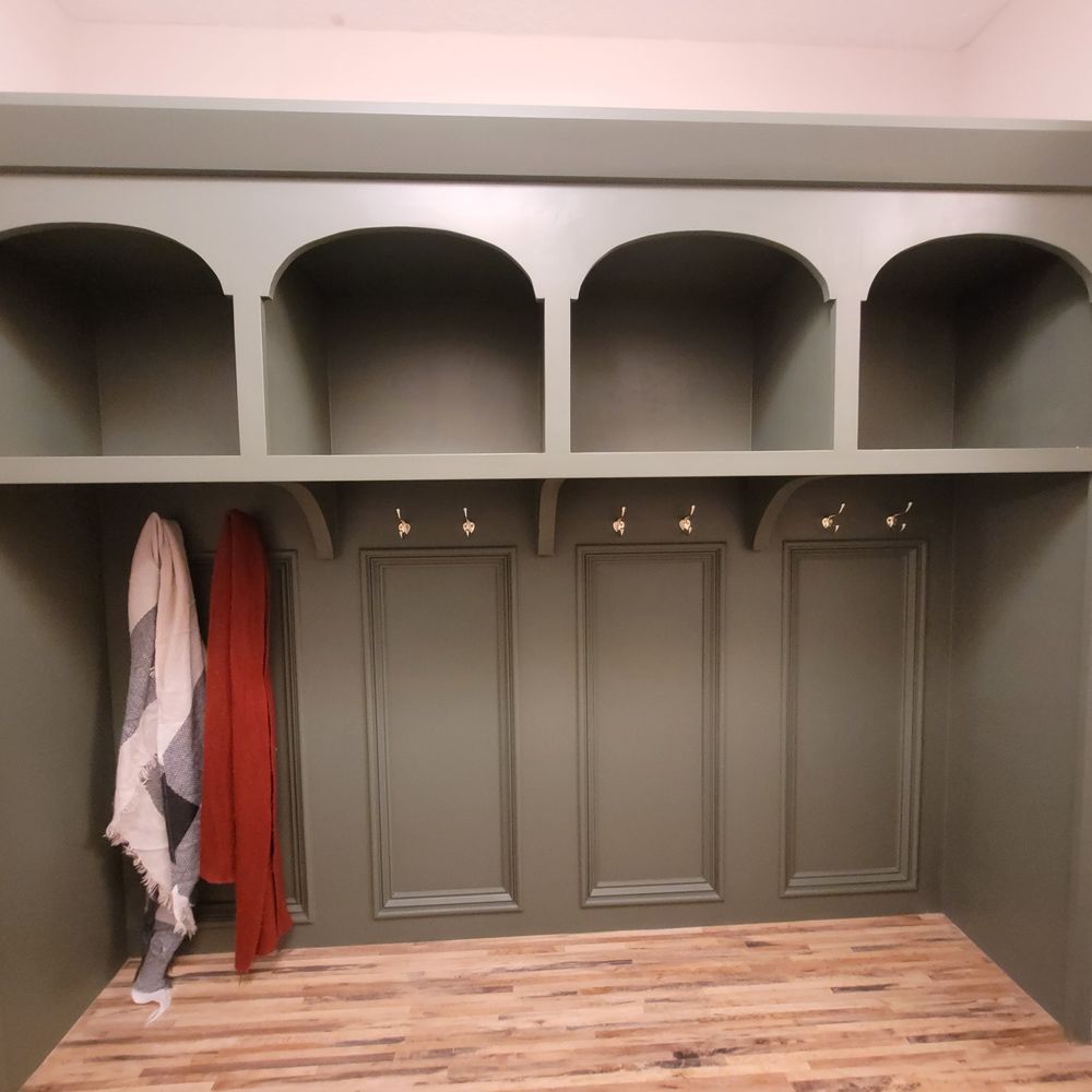 Built-in sage green storage unit with arched cubbies, hooks, and decorative panels. Scarves hang on the hooks.