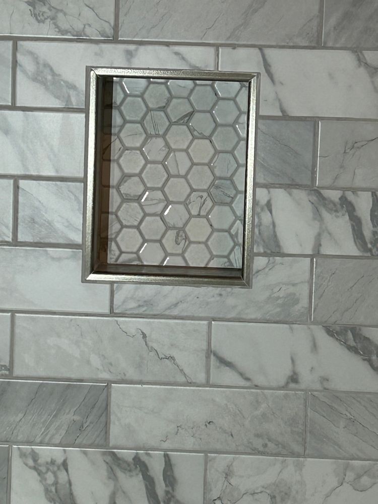 Shower wall with a recessed shelf, gray and white marble tiles, honeycomb tile in the niche.