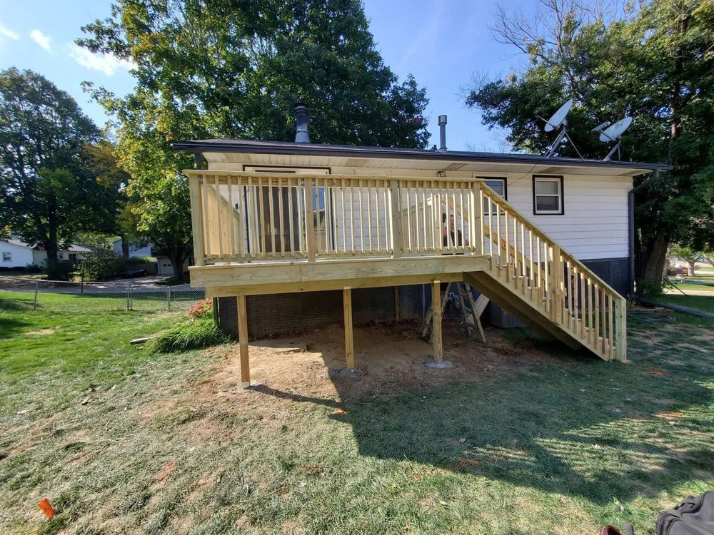Newly built wooden deck with railing and stairs, attached to a white house with green lawn.