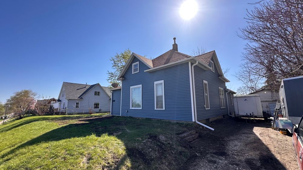 Blue house with white trim on a sunny day. Green grass in front, blue sky.
