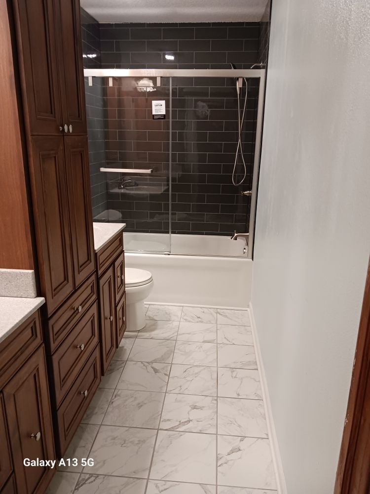 Bathroom with dark tiled shower, white vanity, wooden cabinets, and marble-look flooring.