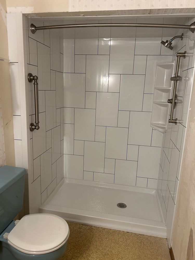 White tiled shower stall with grab bar, shower head, and toilet.