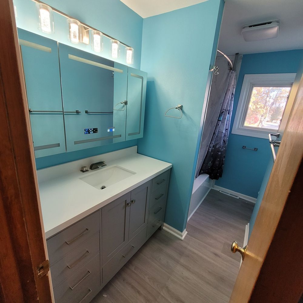 A newly remodeled bathroom with blue walls, a gray vanity, and a shower area.