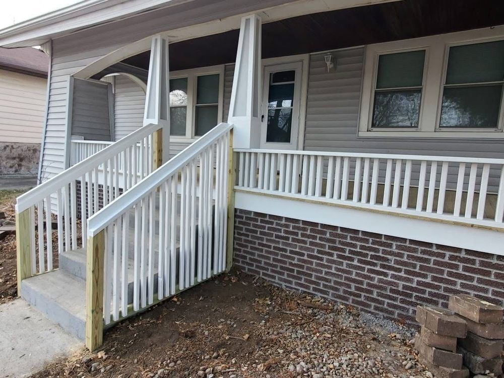 Newly constructed house porch with a white railing and brick base.