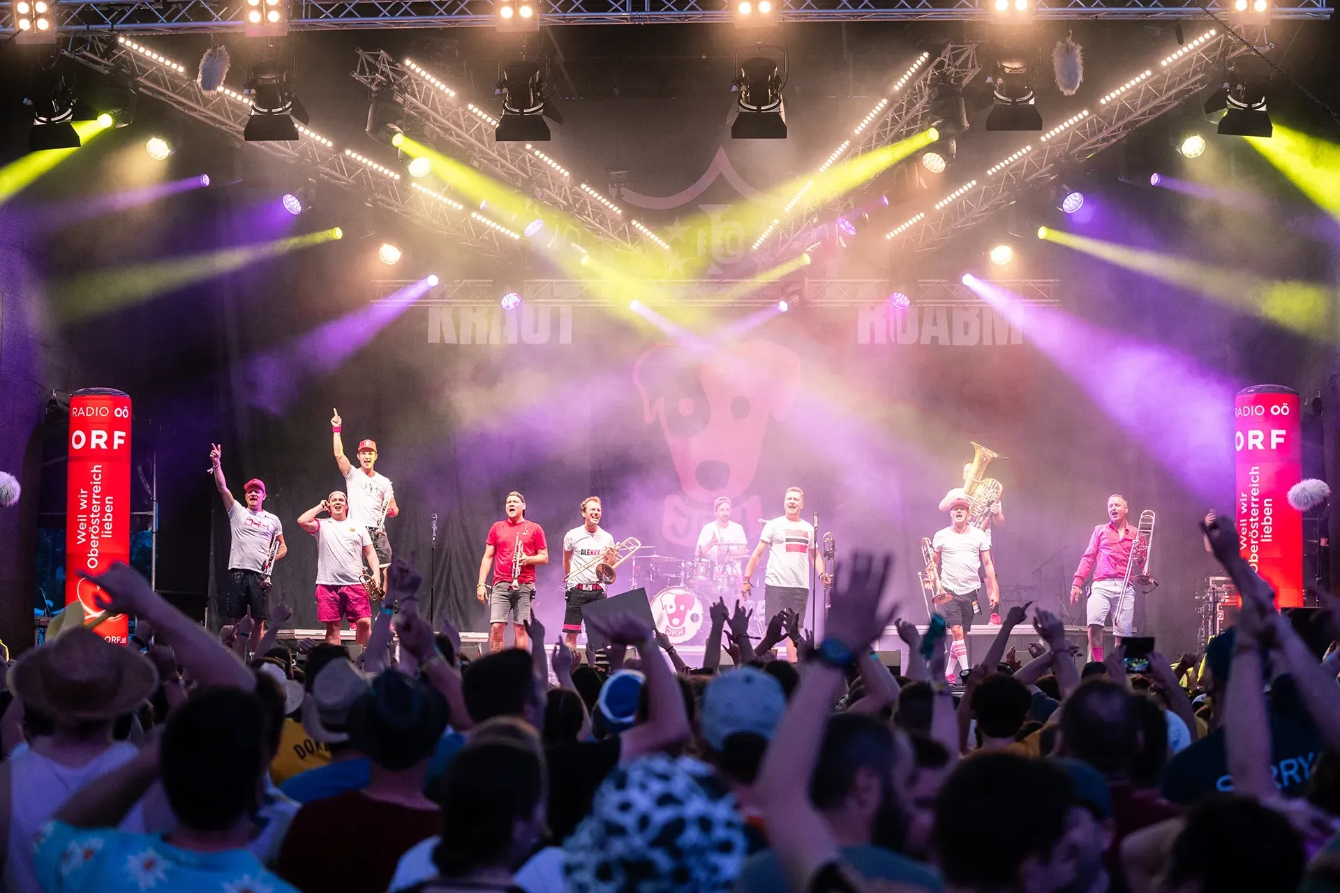 Eine Gruppe von Menschen steht mit erhobenen Händen auf einer Bühne.