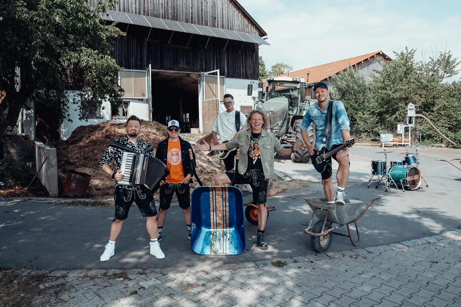 Eine Gruppe von Männern, die Band Troglauer, steht nebeneinander vor einer Scheune.