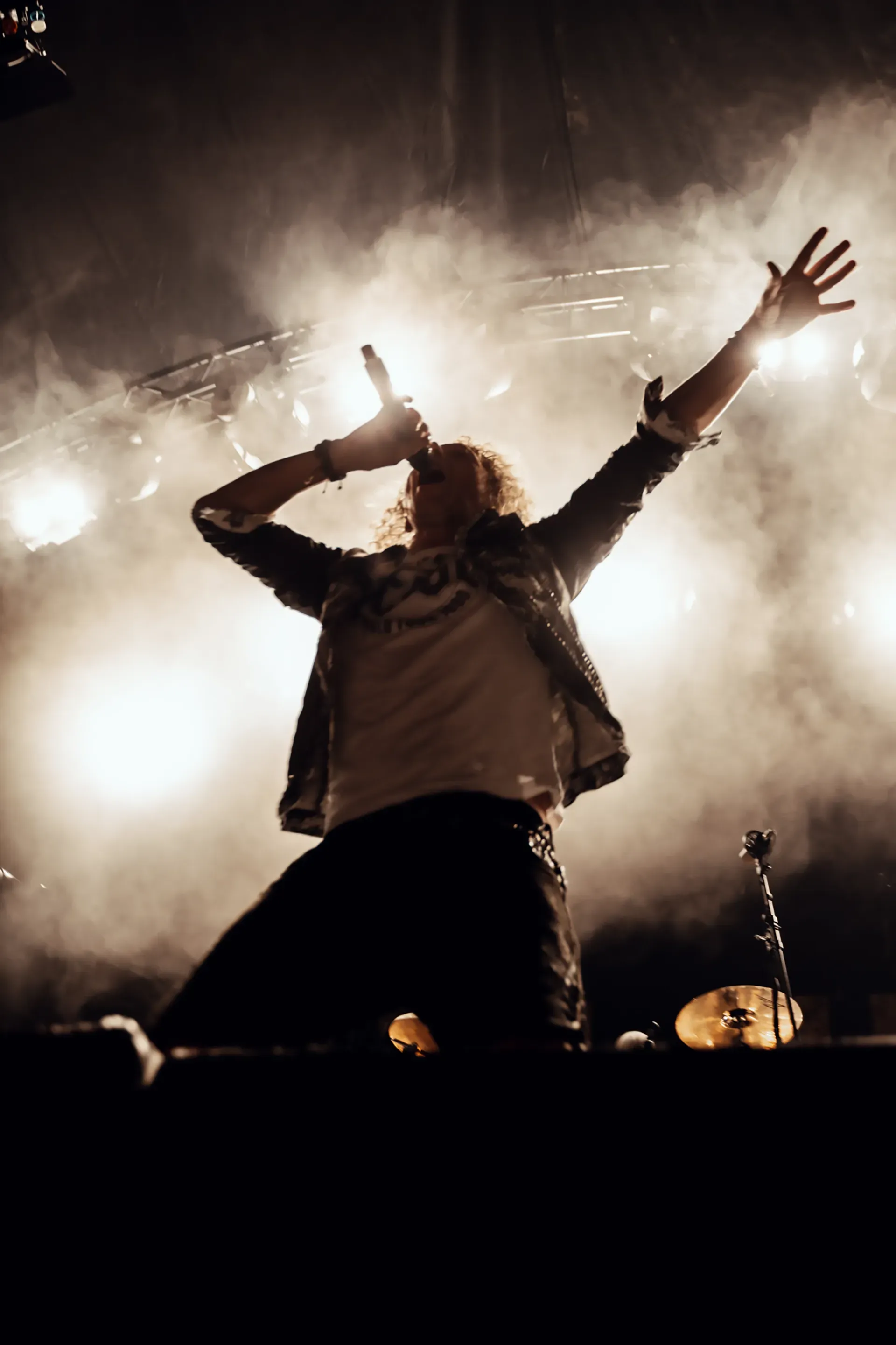 Ein Mann singt mit erhobenen Armen auf einer Bühne in ein Mikrofon.