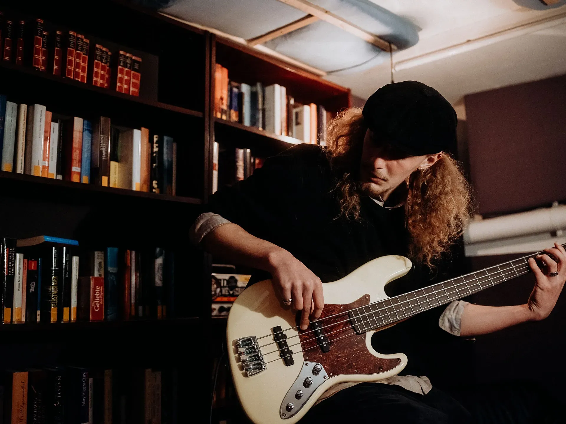 Ein Mann spielt vor einem Bücherregal Bassgitarre.